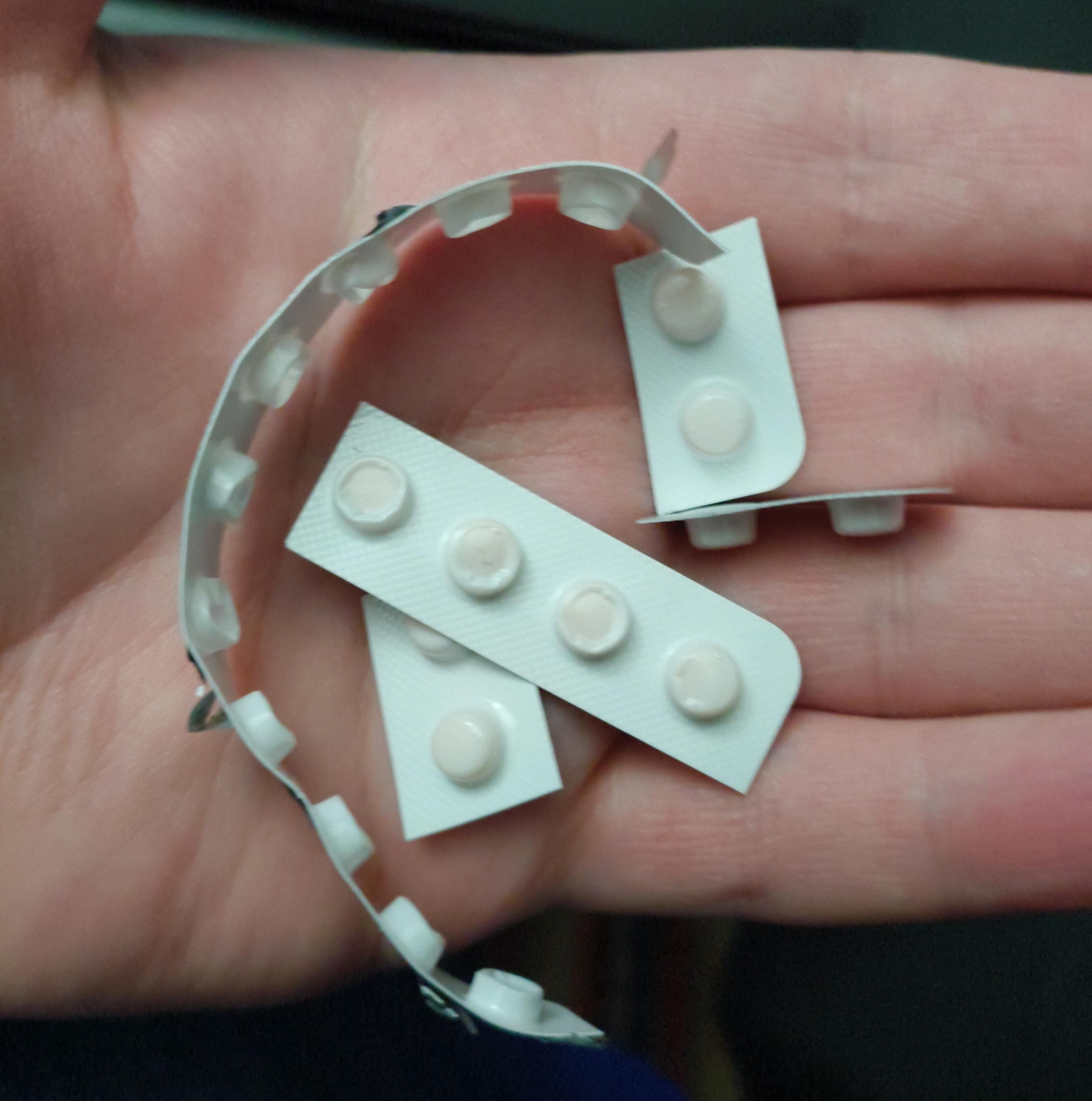 A picture of my hand holding small sections of medication blister pack, cut with scissors to make up the last handful of pills I'm prescribed, with each cut leaving razor-sharp corners and edges