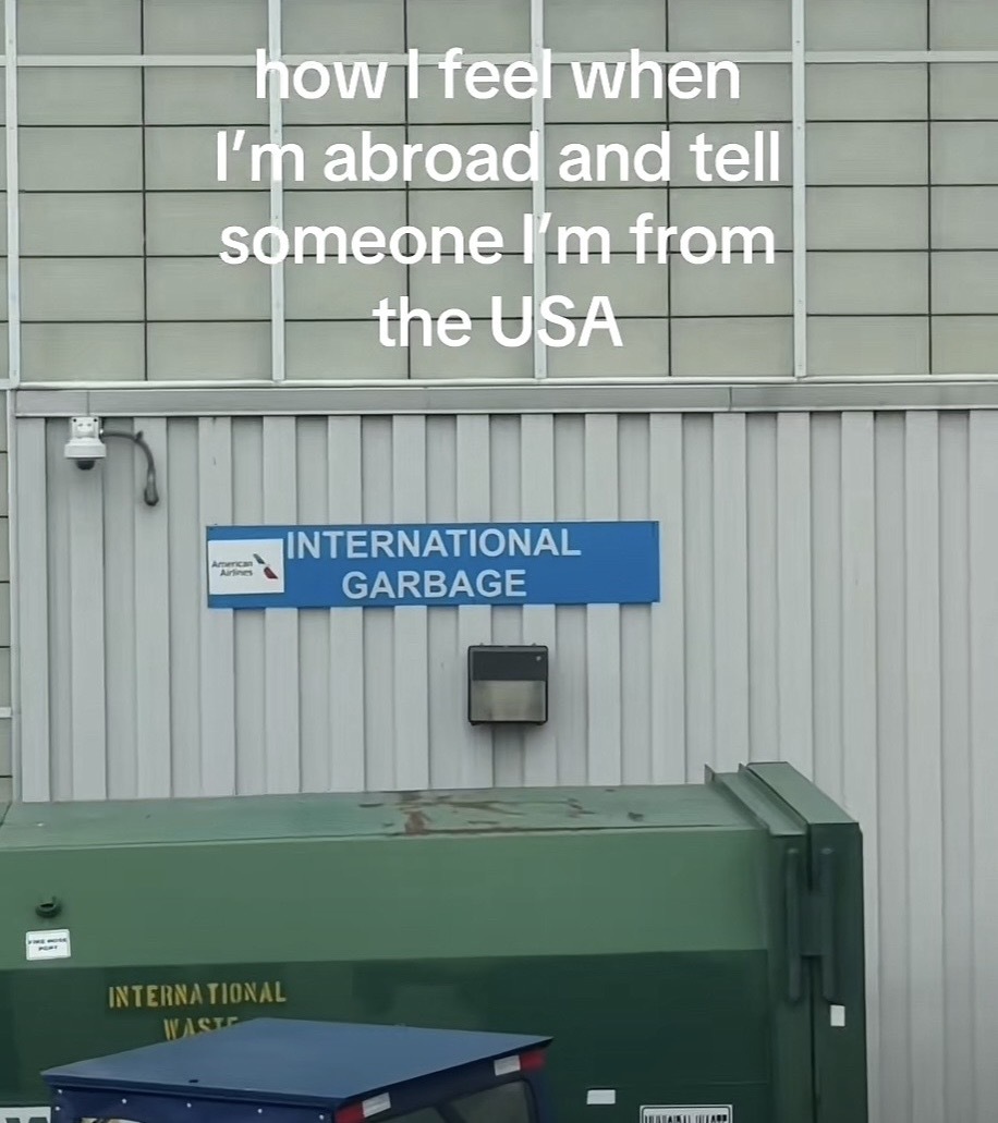 A dumpster labeled “International garbage” on an airport tarmac with the caption “ how feel when I'm abroad and tell someone I'm from the USA”